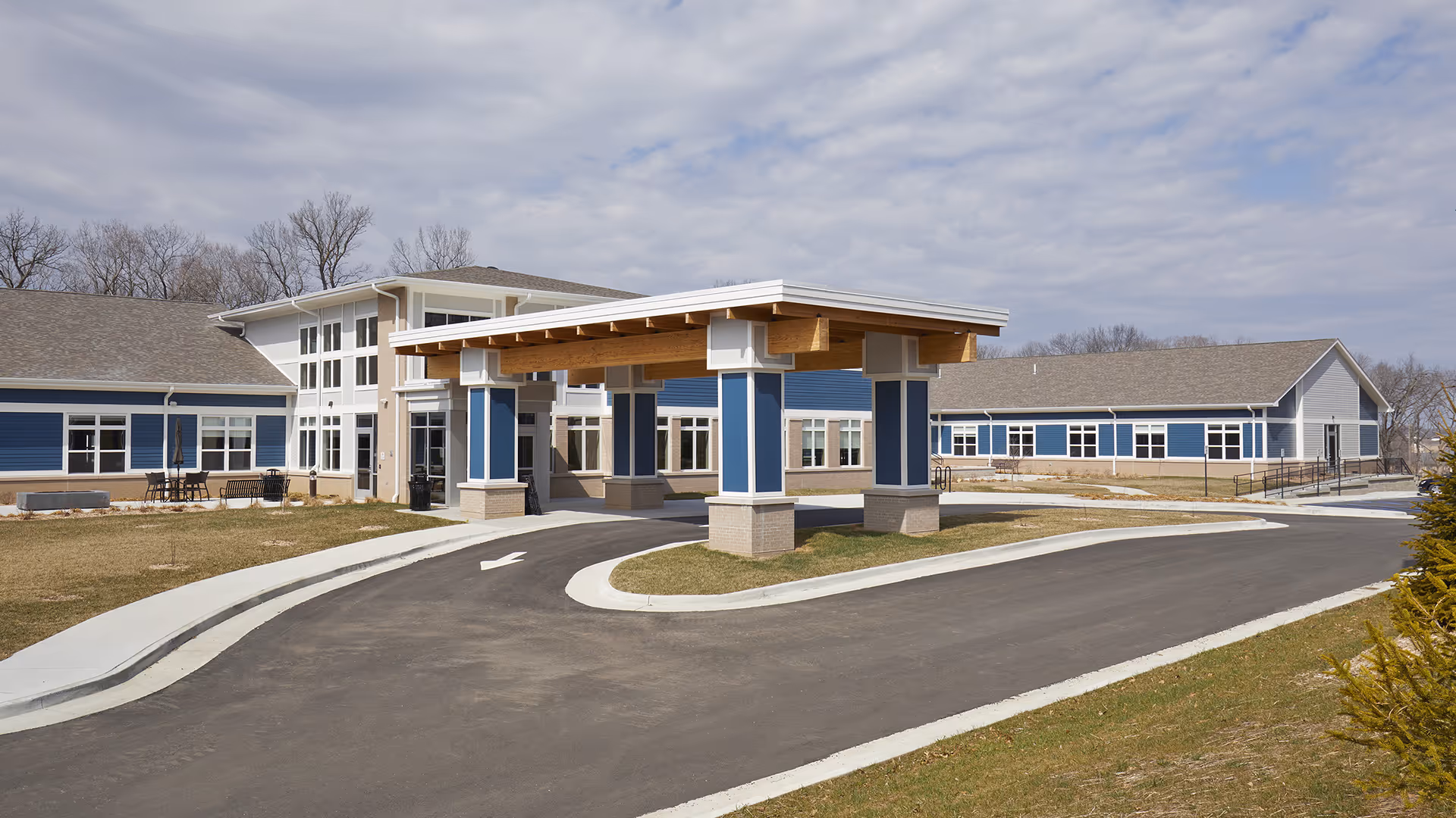 Front exterior of a blue-and-white senior living facility with a covered entrance and circular driveway.
