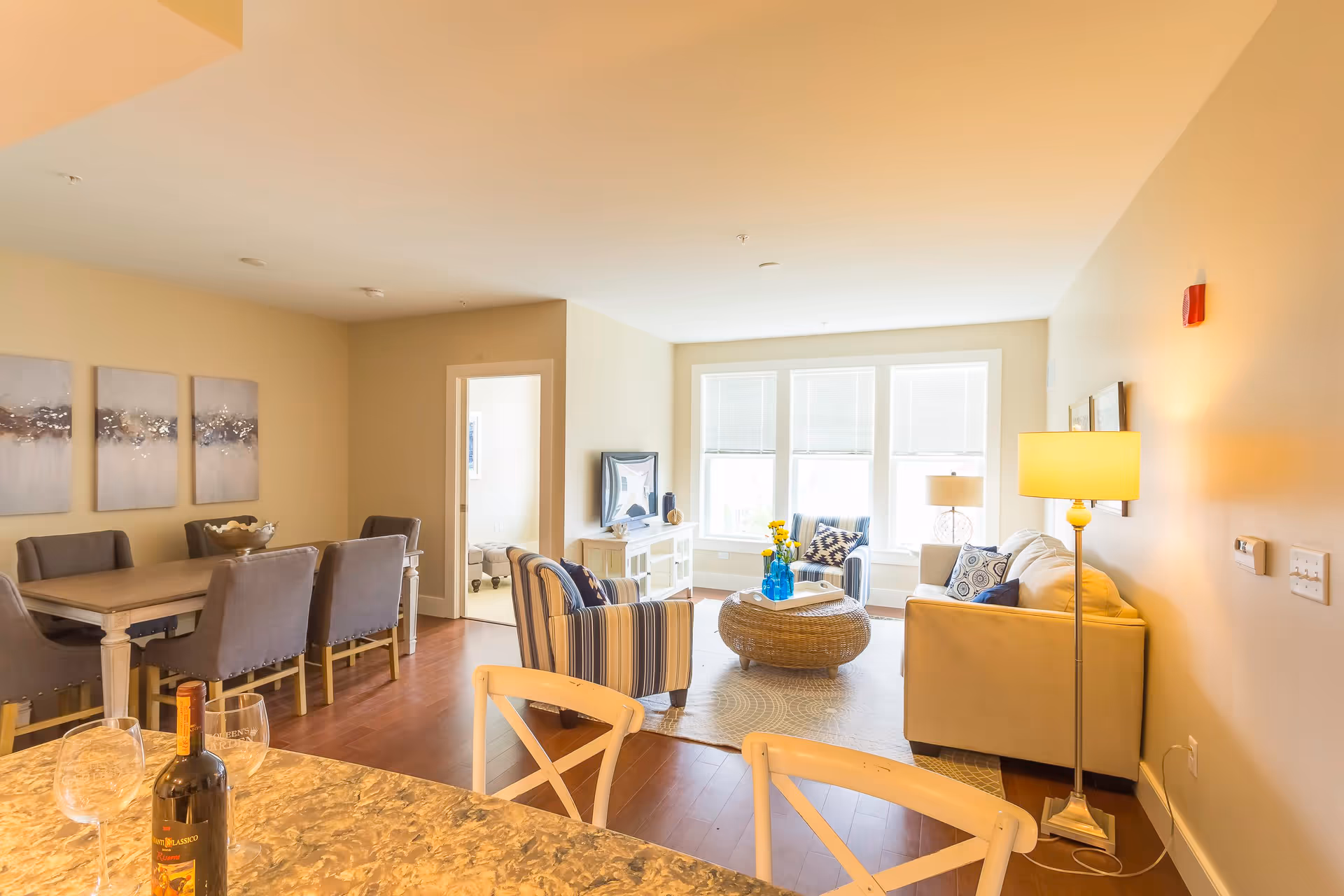 Bright open-plan living and dining area with sofas, armchairs, a dining table, and large windows.