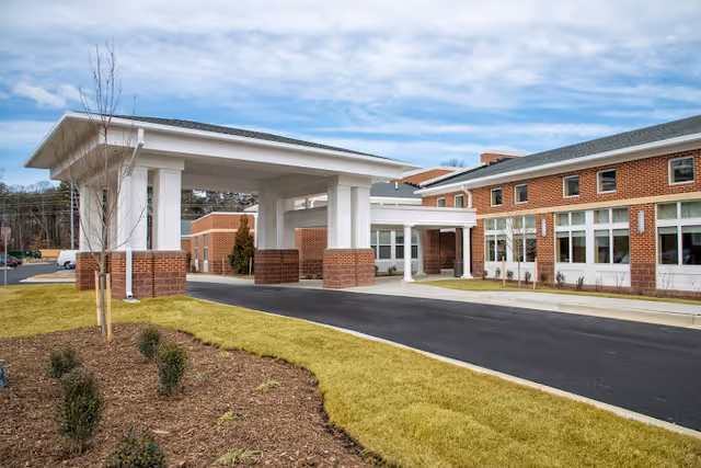Front entrance of a brick rehabilitation center with a covered porte-cochere, driveway, and landscaped lawn.