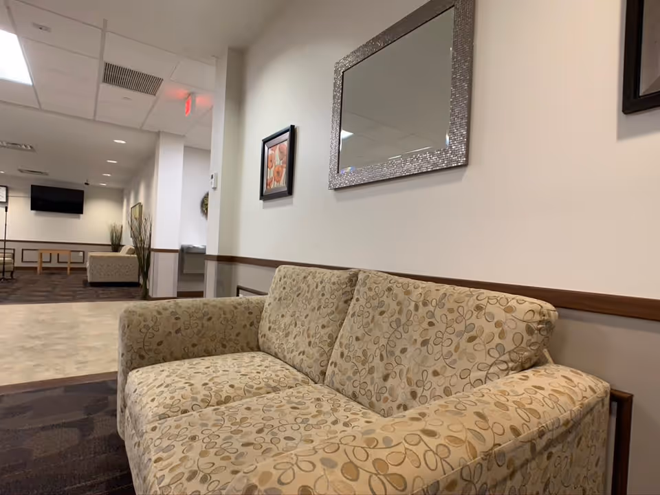 A cozy sofa with a floral pattern in a lobby area, featuring a decorative mirror and framed artwork on the wall.