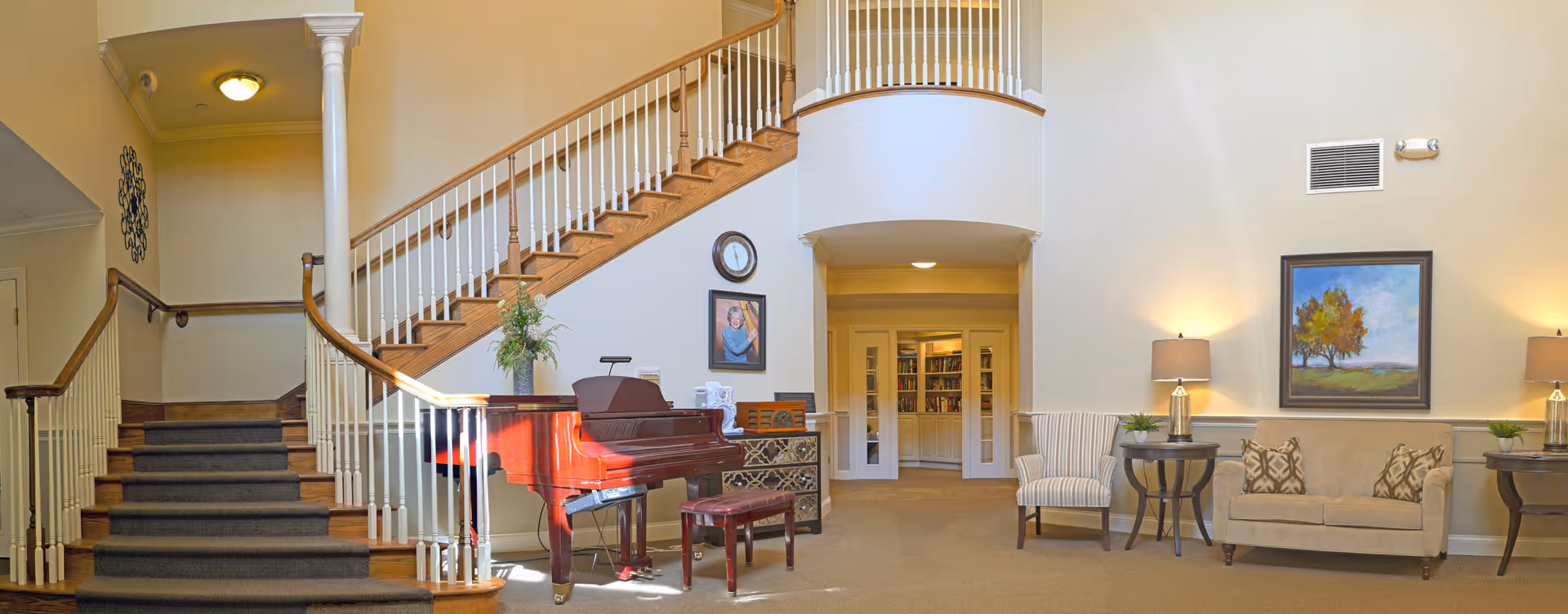 Spacious interior common area with a curved staircase, a red grand piano, and seating including chairs and a sofa.