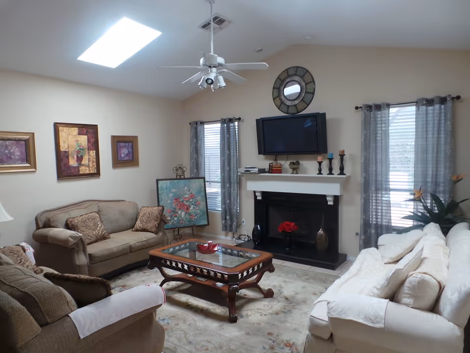 Bright living room with sofas, a wooden coffee table, a fireplace with a TV above, and framed wall art.