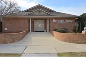 Brick single-story building entrance with double doors, columns, curved brick planters and a sign reading "Heritage Home of Florence, Inc."