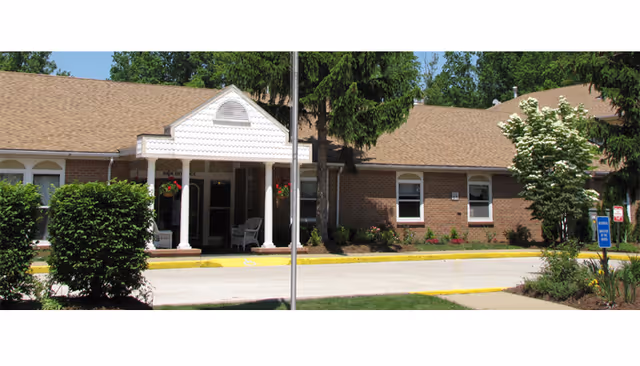 Brick senior living facility with front entrance, white columns, and landscaped surroundings.