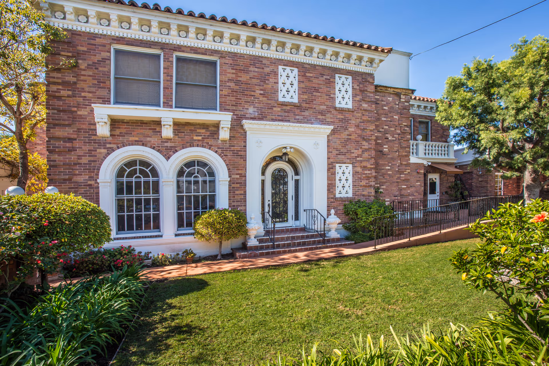 Brick two-story building with arched windows, an ornate arched entrance and a manicured lawn and walkway in front.