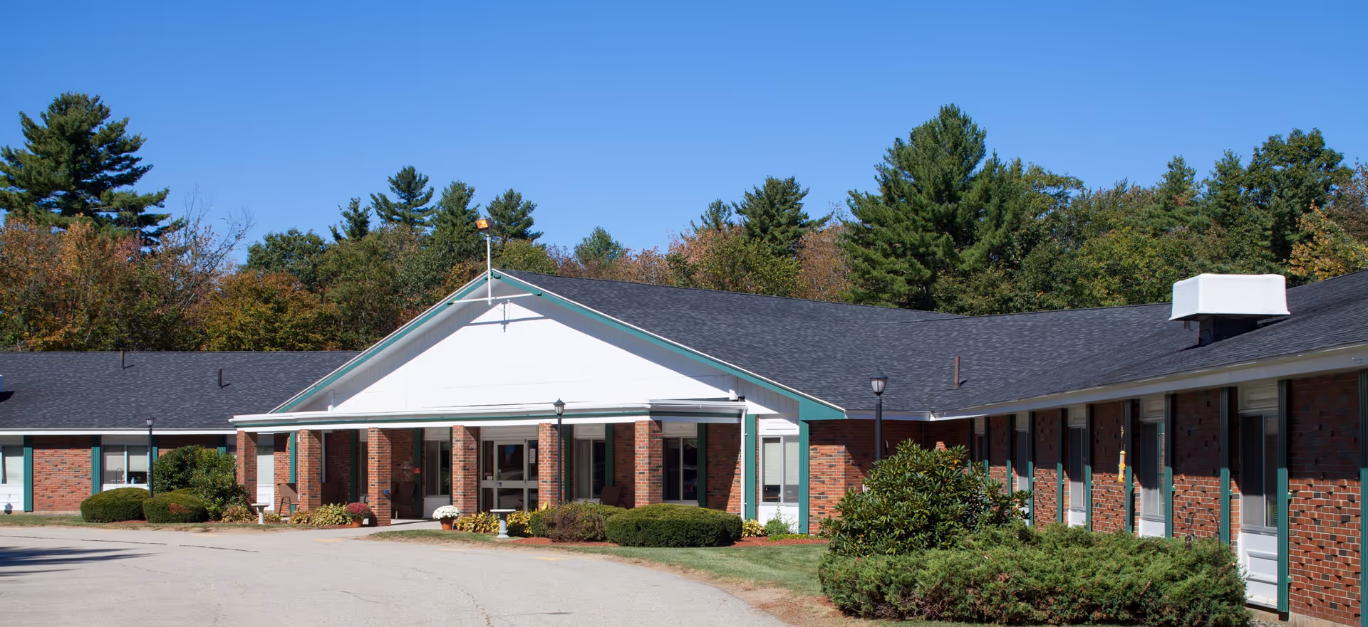 Single-story brick building with a covered entrance, landscaped shrubs, and a circular driveway under a clear blue sky.