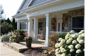 Front view of a senior living center featuring a covered entrance, columns, and white hydrangeas.