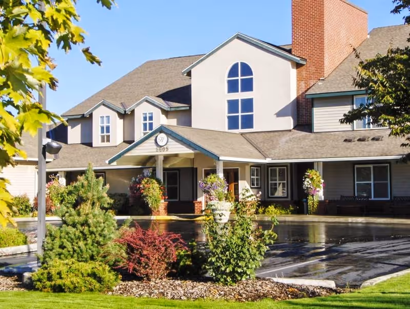 Front exterior of a senior living building with a covered entrance, landscaped grounds, and large windows.