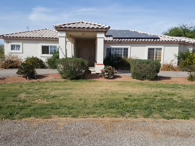 A single-story assisted living home exterior with a covered entrance and manicured shrubs.