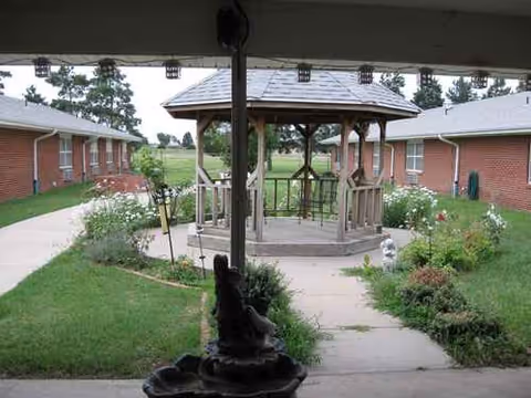 Outdoor courtyard with a gazebo between brick buildings, garden beds, and paved walkways.