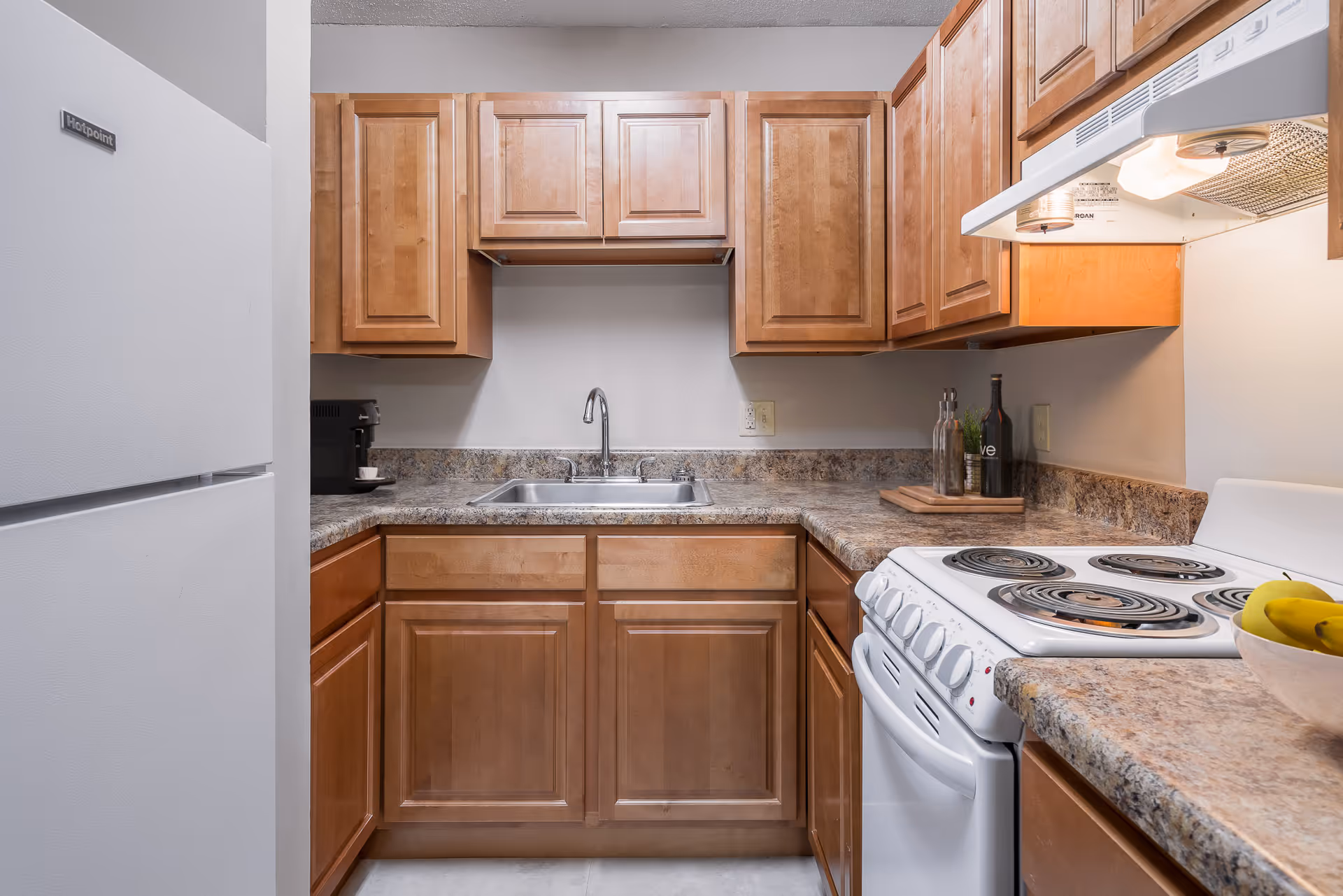Compact kitchen with wooden cabinets, a sink, white refrigerator and electric stove on a laminate countertop.
