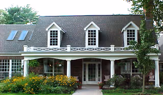 Brick two-story building front with a covered columned porch, three dormer windows, skylights, and landscaped flower beds.