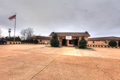 Brick healthcare facility with central entrance, surrounding parking lot, and a waving American flag.