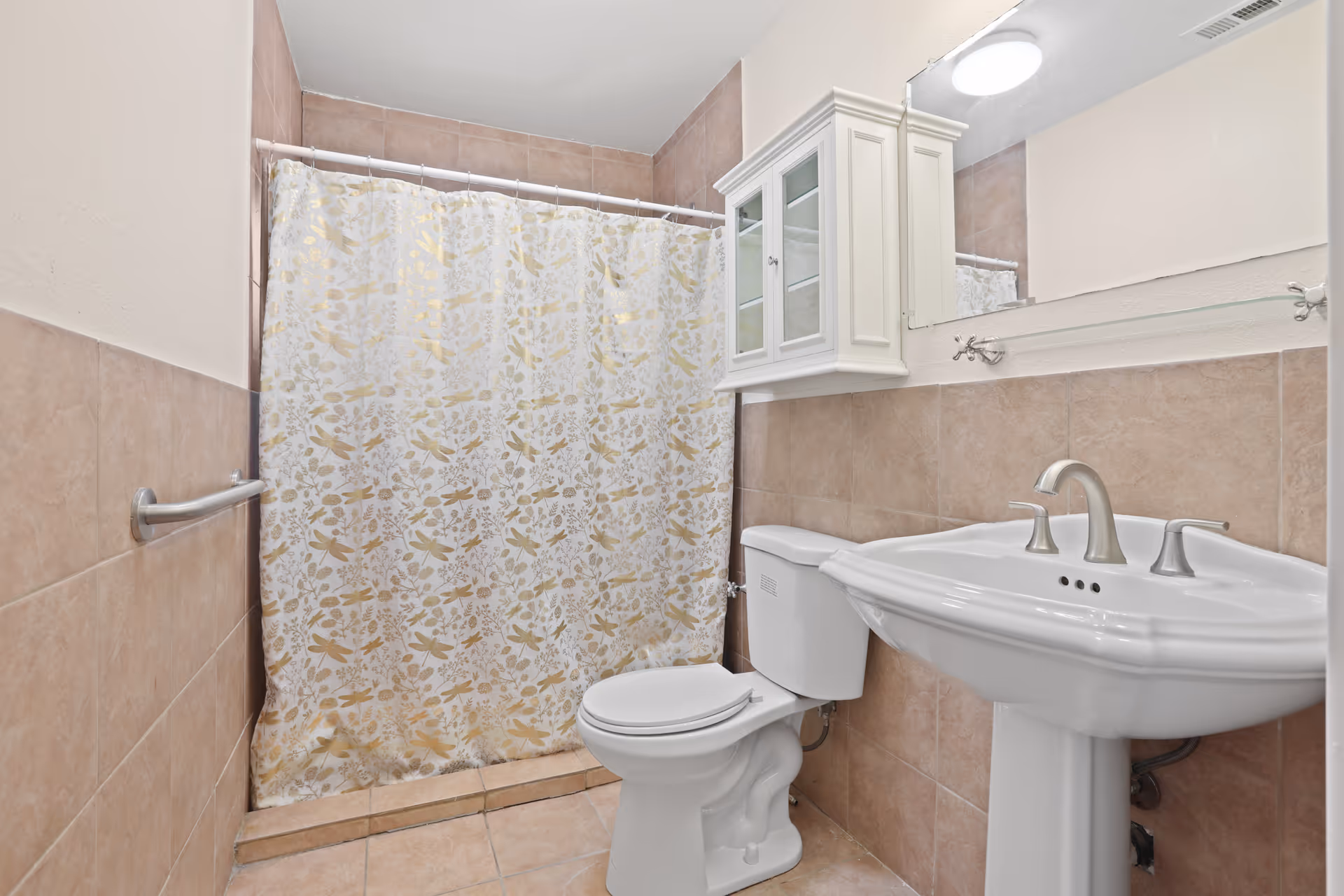 Small tiled bathroom with a patterned shower curtain, toilet, pedestal sink, and wall-mounted medicine cabinet.
