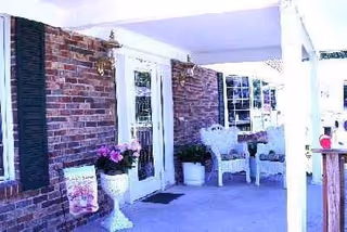 Brick facility exterior with a covered porch, white chairs, and potted plants.