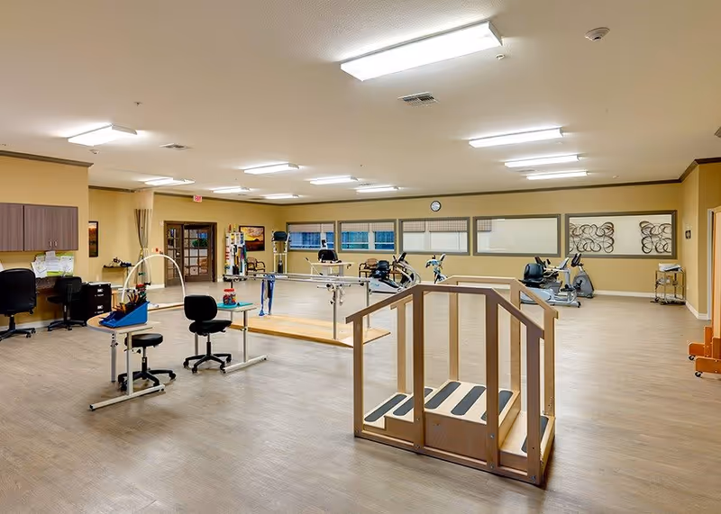 Spacious indoor rehabilitation/exercise room with parallel bars, practice stairs, exercise bikes, and therapy workstations.