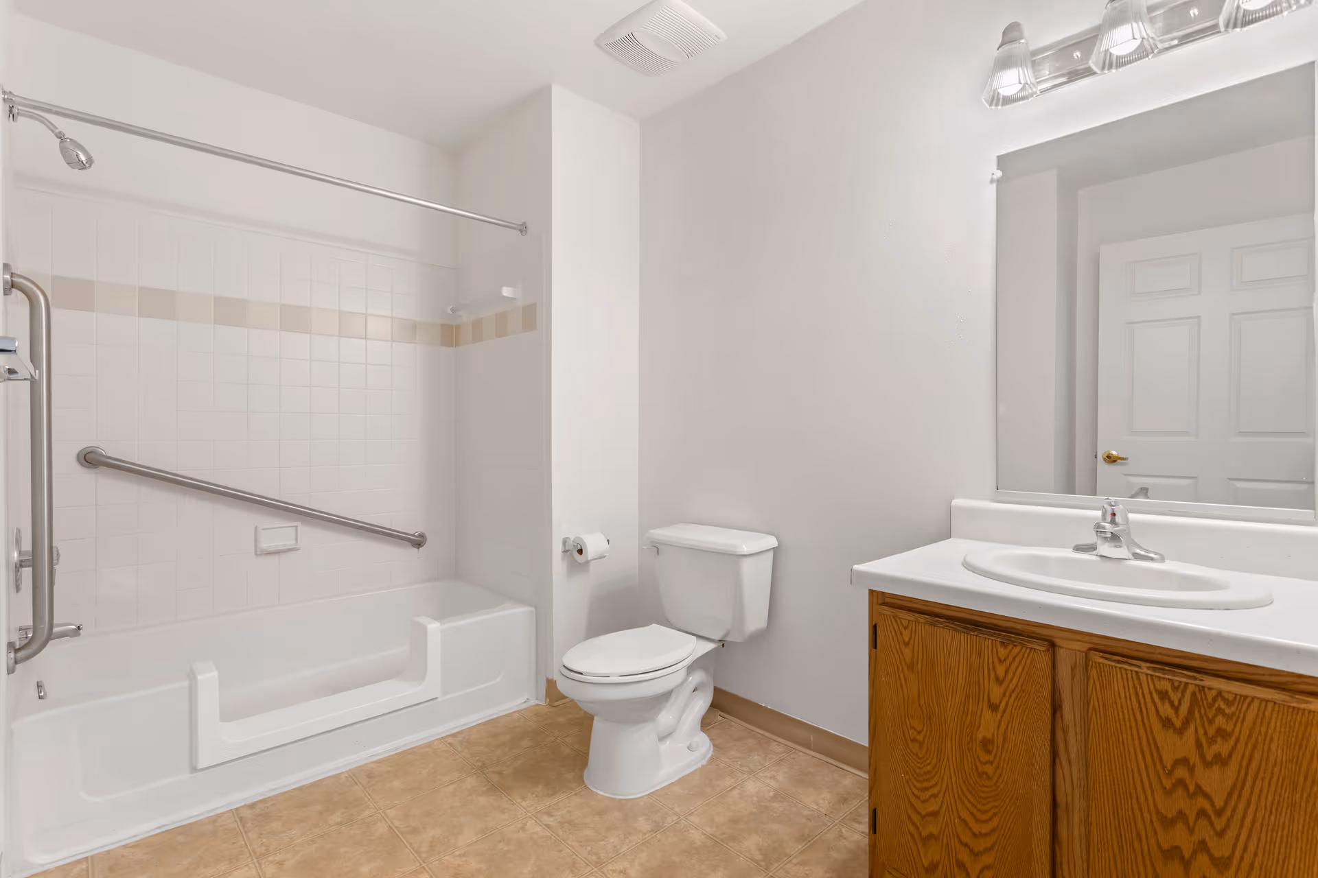 Bathroom with a bathtub/shower with grab bars, a toilet, and a sink with a wooden vanity and mirror.