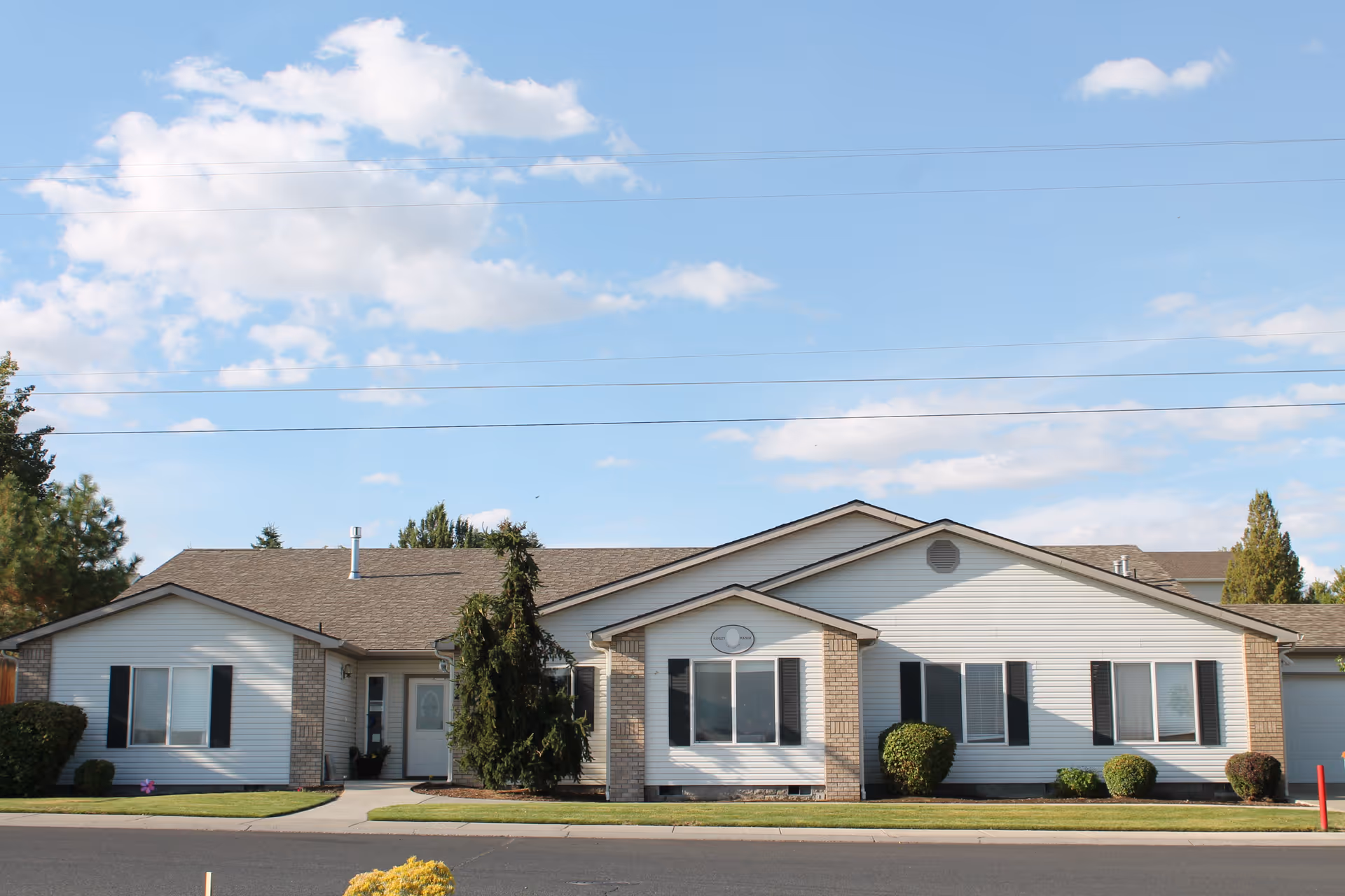 Single-story white-sided building with brick accents, windows, shrubs and a manicured lawn under a blue sky.