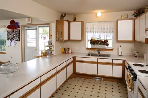 U-shaped white kitchen with brown-trim cabinets, sink, stove, and a windowed breakfast area.