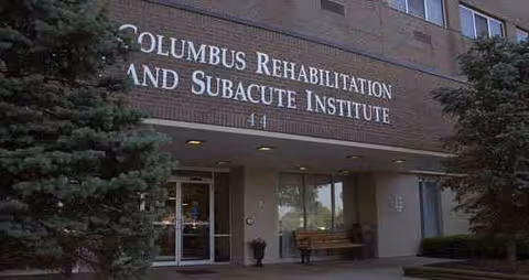 Exterior view of a brick building entrance with a sign and bench.