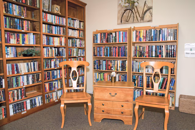 Small library/reading area with wooden bookshelves filled with books, two wooden chairs, and a small wooden side table.