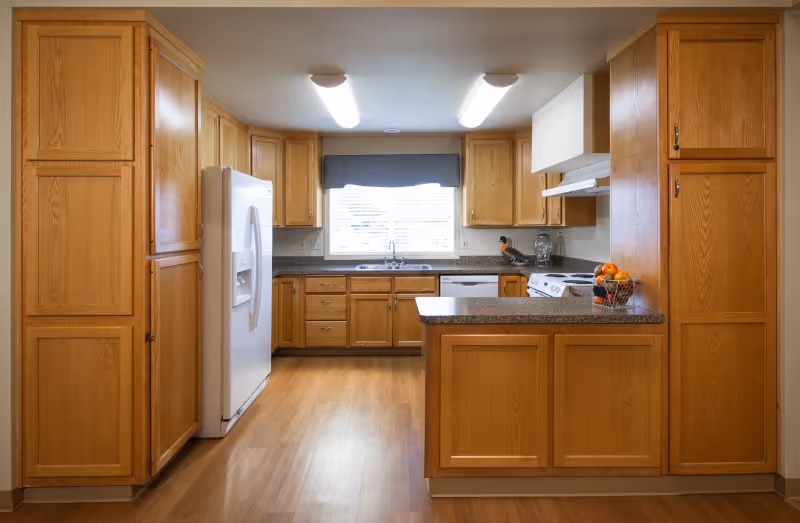 Bright kitchen with oak cabinets, a white refrigerator, an island countertop, sink beneath a window, and a stove.