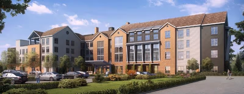 Exterior view of a multi-story senior living facility named Tribute at The Glen, featuring a mix of brick and siding facade, large windows, a covered entrance, landscaped greenery, parked cars, and a few people walking nearby under a partly cloudy sky.