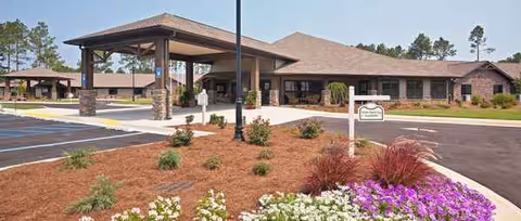 Single-story senior living building with a covered entrance, parking, and landscaped front garden.