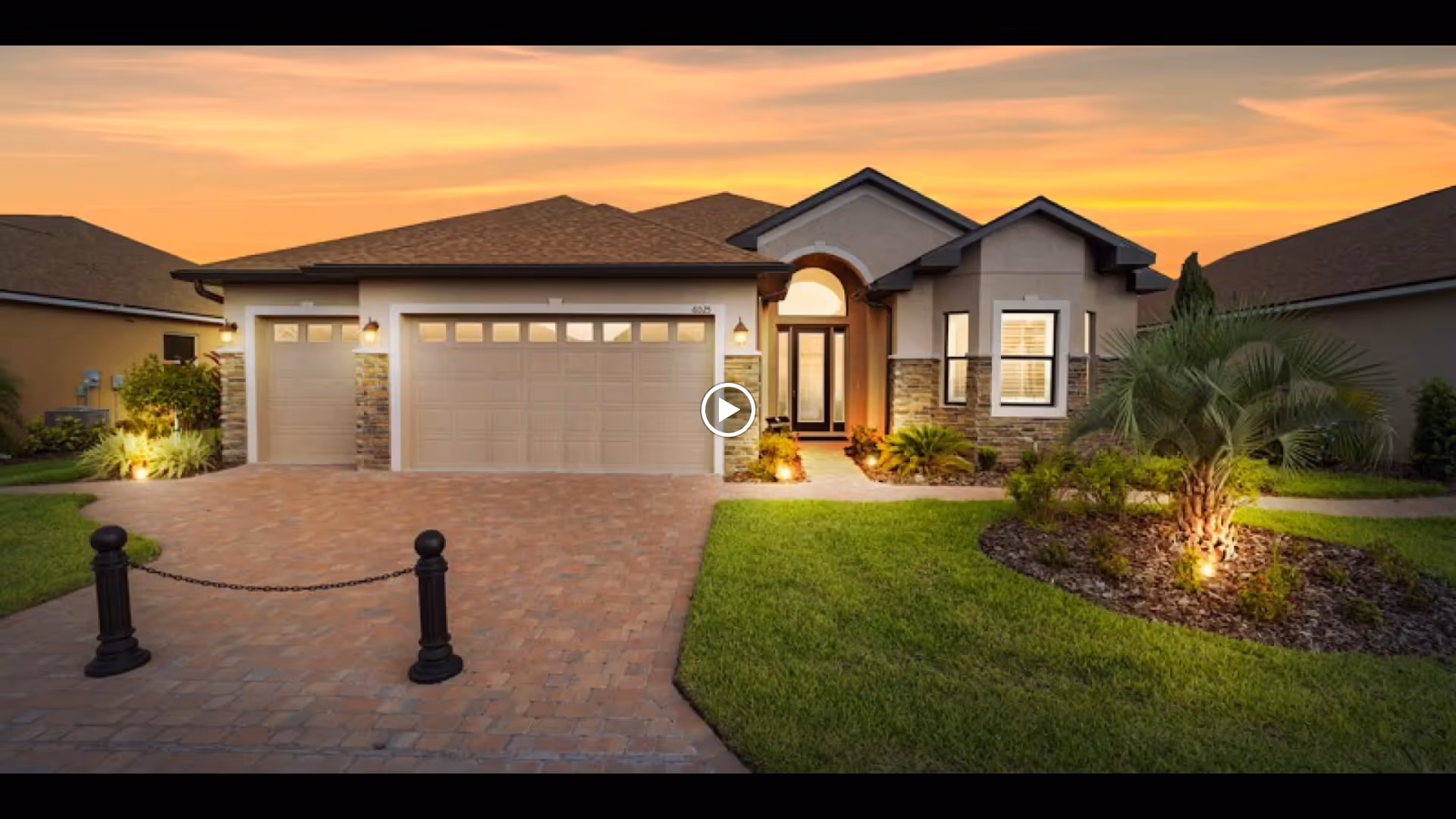 Front exterior of a single-story house with a three-car garage, paved driveway and landscaped yard at sunset.