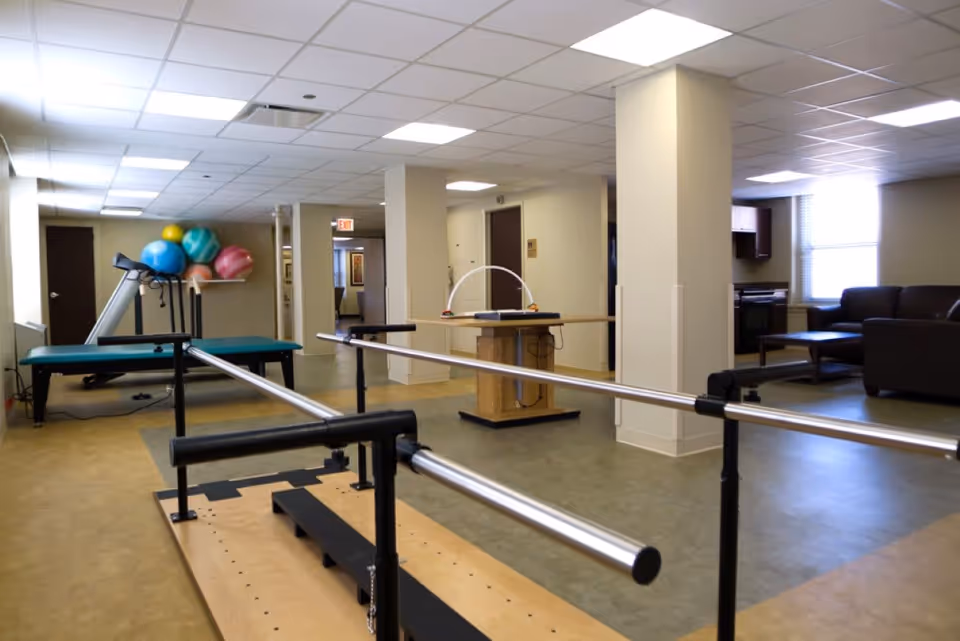 A spacious interior therapy and exercise room with parallel bars, a treadmill, exercise balls and seating.