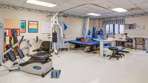 Rehabilitation gym in a senior facility with exercise equipment and therapy beds.