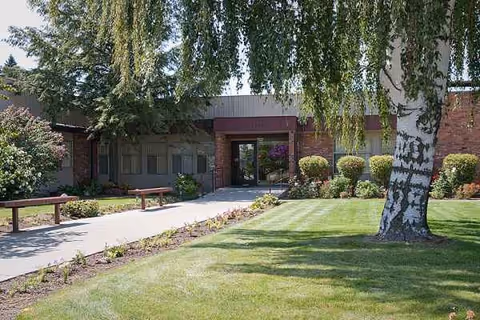 Front view of Gardens on University facility with brick entrance, path, benches, and landscaping.