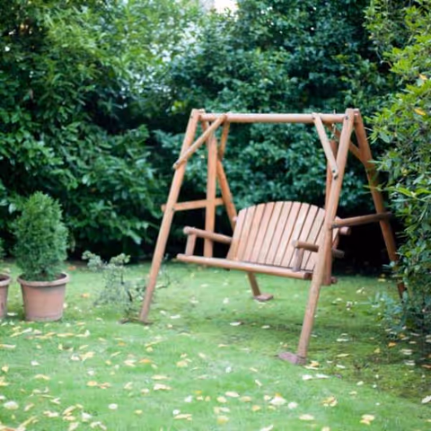 Wooden garden swing on a grassy lawn with trees and potted plants.