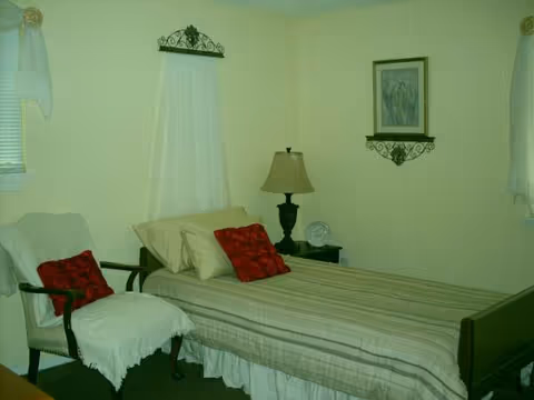 A cozy bedroom with a striped bed, two chairs, and a bedside lamp.