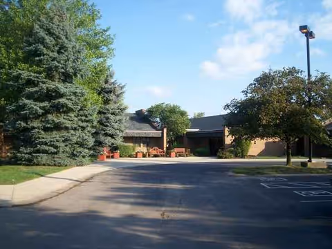Exterior view of Willowbend Living Center with driveway, trees, and outdoor seating by the entrance.