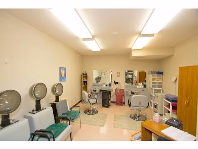 Small salon room with hooded hair dryers, styling chairs, mirrors and storage cabinets.