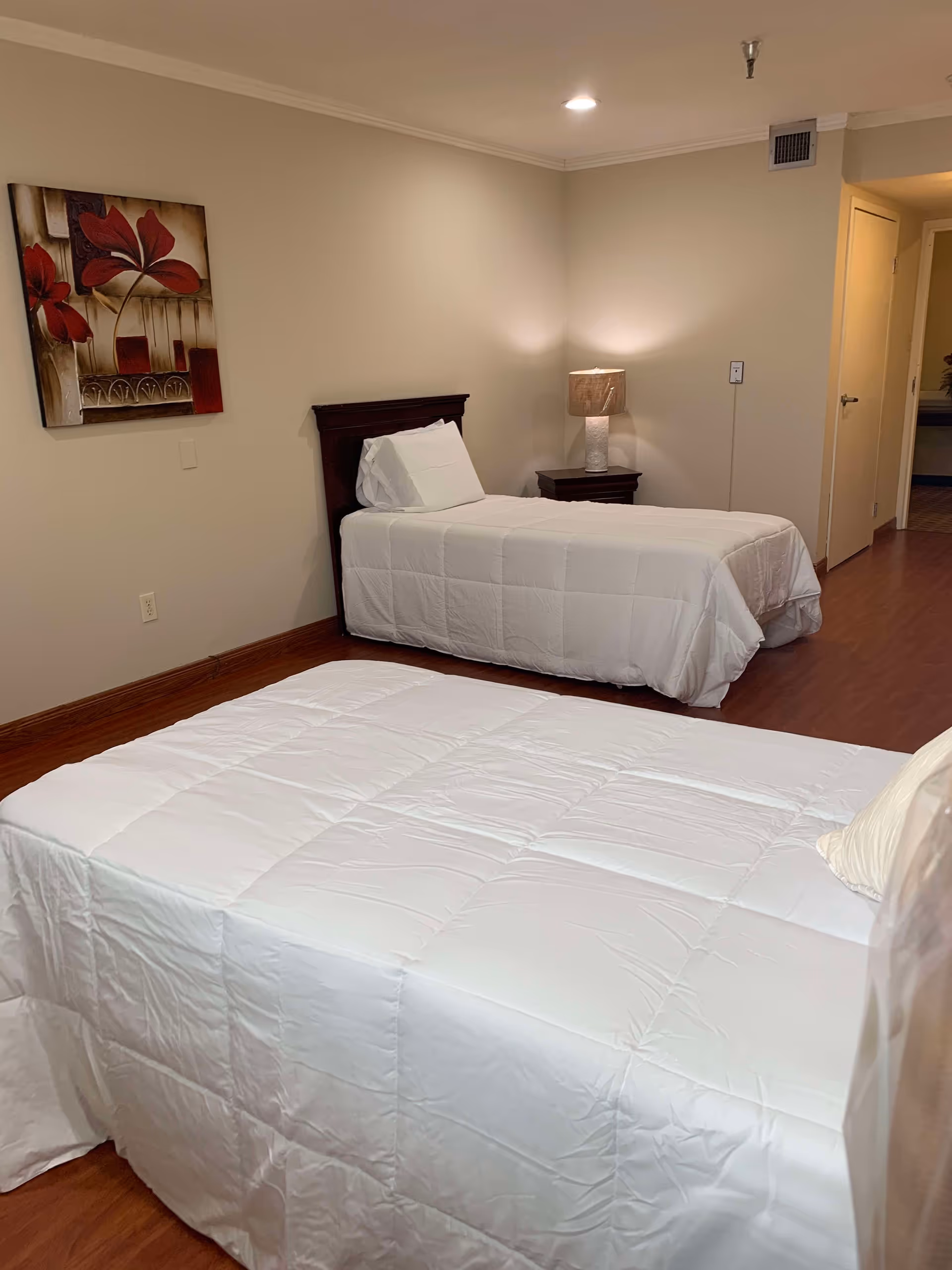 A clean shared bedroom with two single beds, a nightstand with a lamp, and wall art.