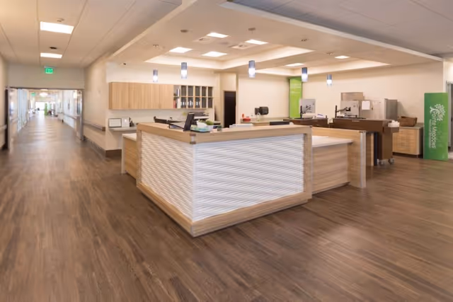 Reception desk and open hallway inside a senior living facility with wood floors and pendant lights.