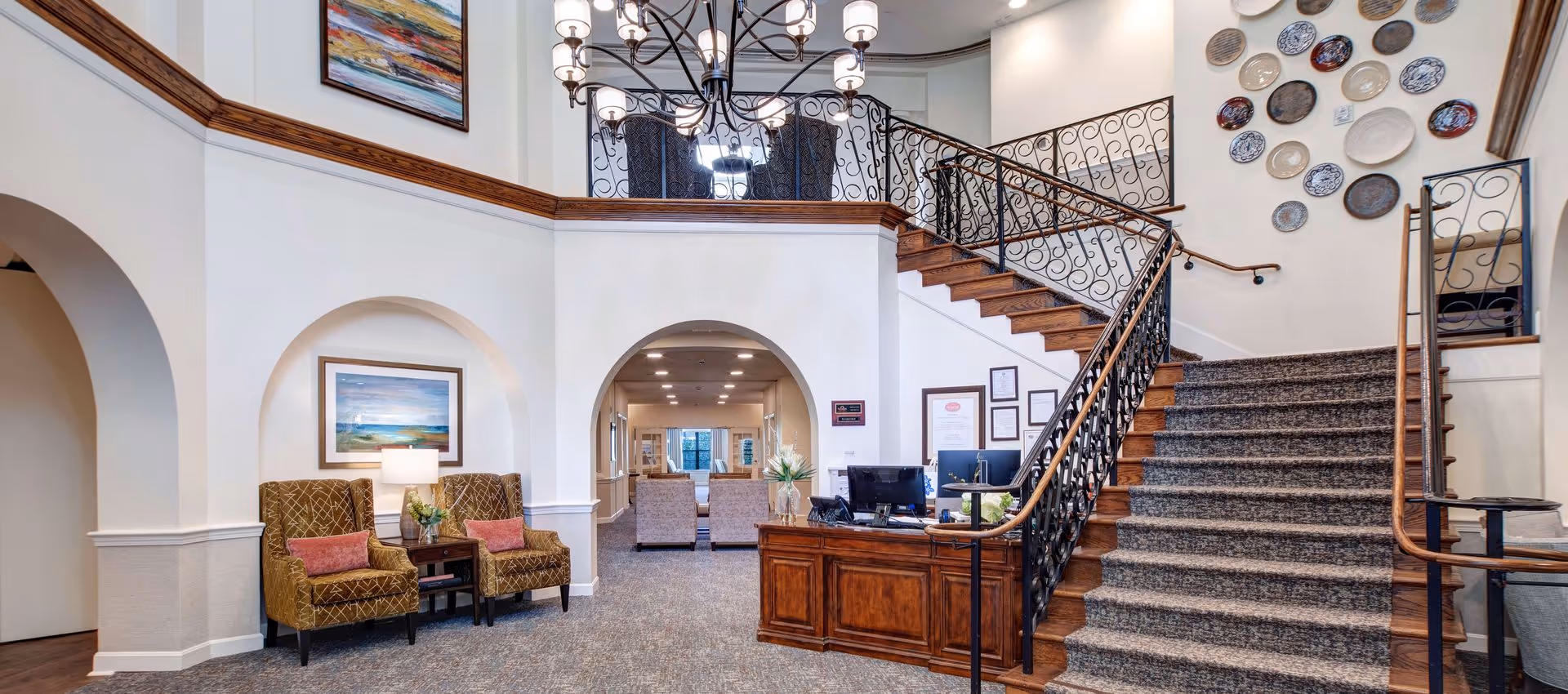 Lobby interior with a carpeted staircase, wooden reception desk, and seating area beneath arched openings.