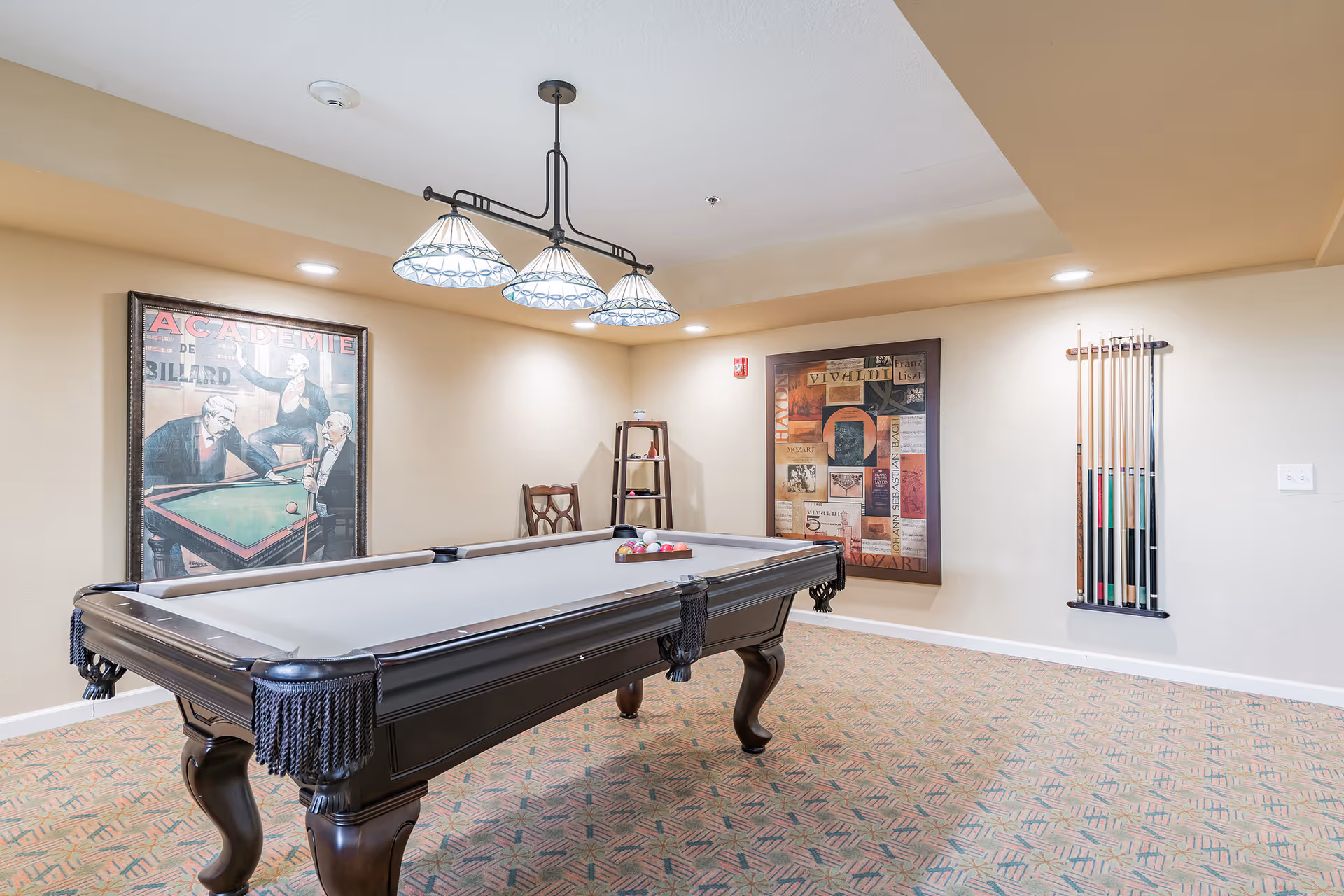 A pool table in a well-lit game room with overhead lights, wall art, and a cue rack.