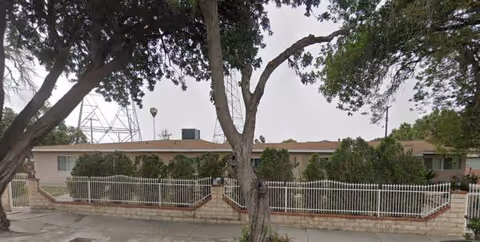 Exterior view of Rinaldi Guest Home with trees, low building, and white rail fence.