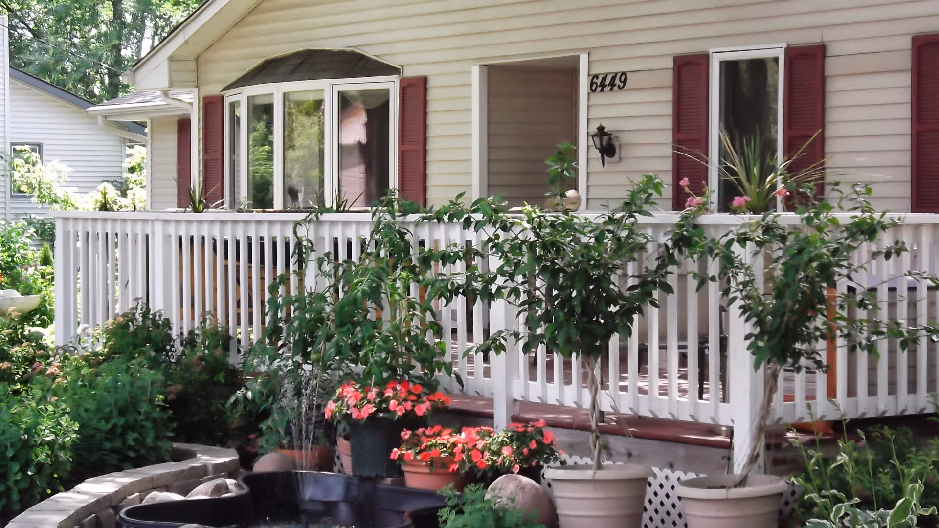 Front porch and railing of a house with potted plants, a small fountain, and the house number 6449.