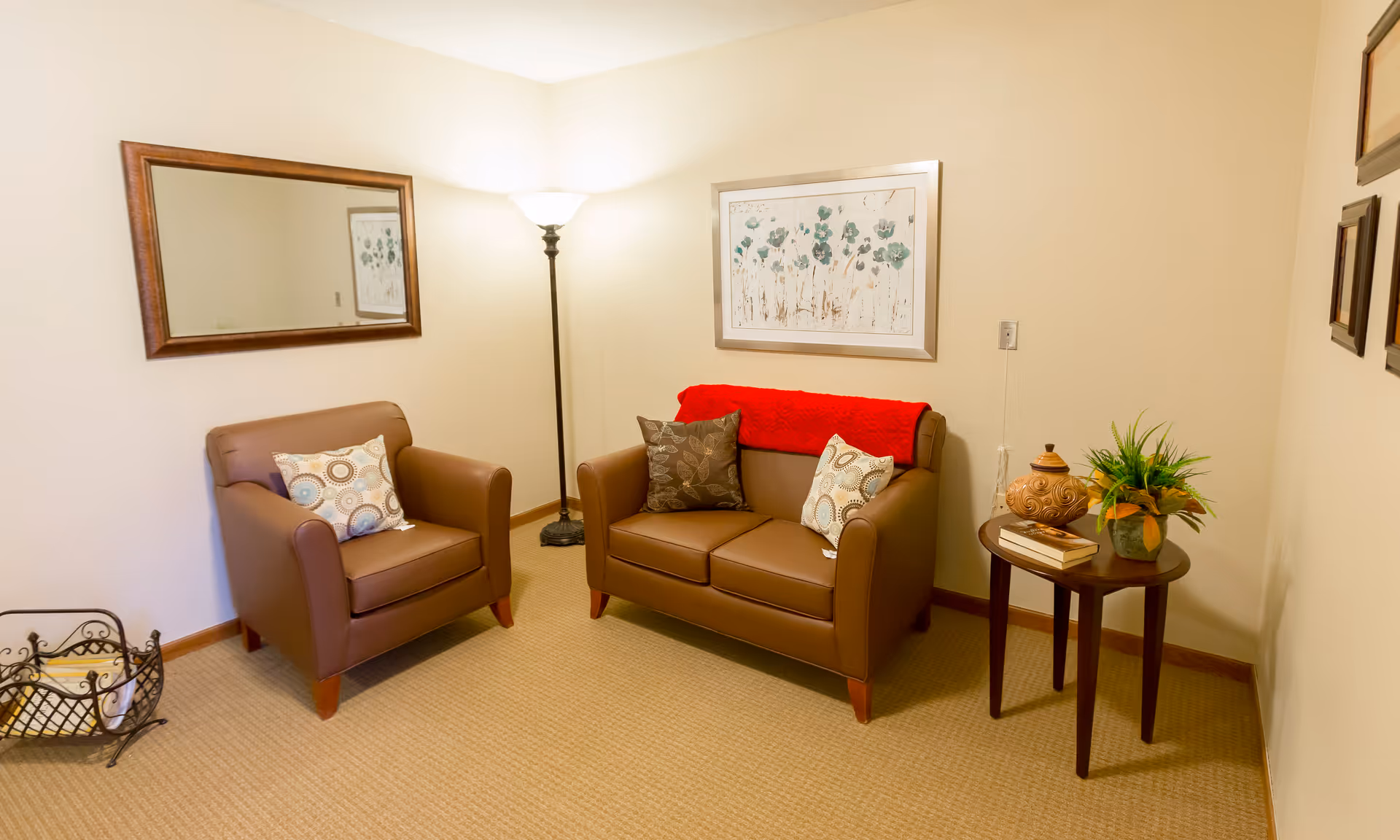 Cozy sitting area with two brown leather armchairs and a matching loveseat, a side table with a plant and lamp, and framed wall art.