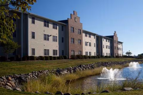 Exterior view of Independence Village of Pella with a brick-front building by a pond.