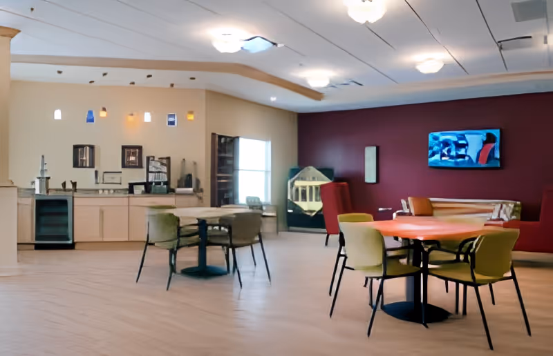 Spacious dining and lounge area with round tables and chairs, a serving counter, and a wall-mounted TV.
