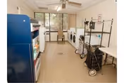 Laundry room with washers and dryers lining one wall, a laundry cart and shelving, a vending machine, and windows at the far end.