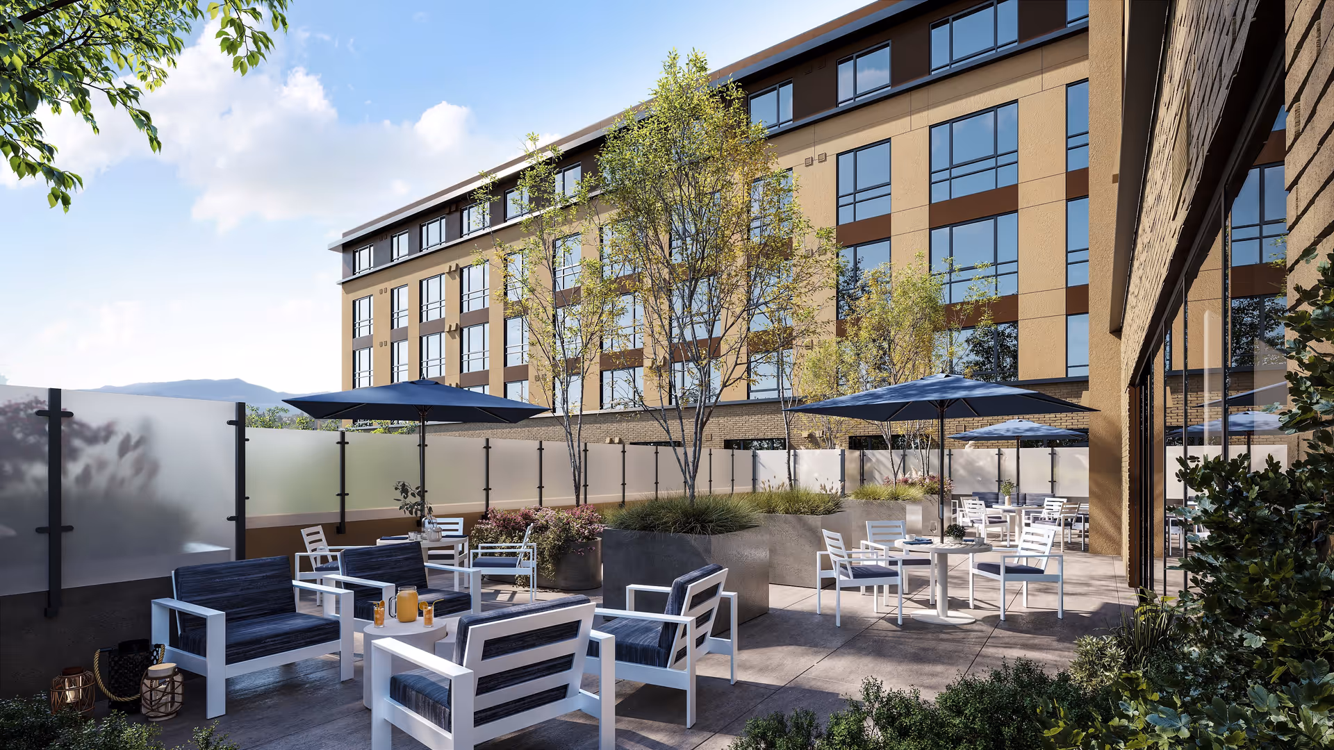Outdoor patio area at The Ivy at Berkeley with modern white and navy blue seating, tables with umbrellas, large planters with trees and shrubs, and a multi-story building in the background under a partly cloudy sky.