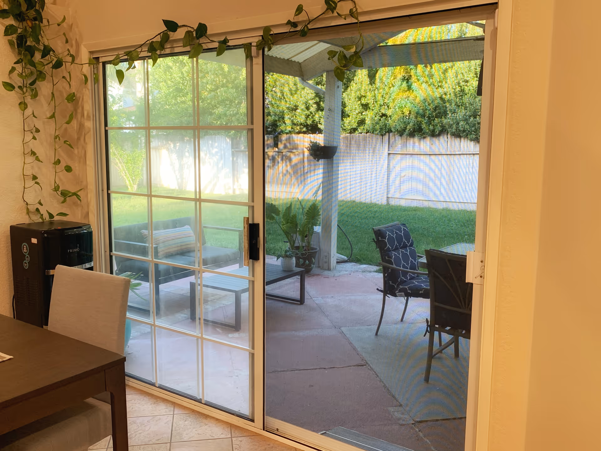 Sliding glass patio door from a dining area looking out onto a backyard patio with chairs, a coffee table, and plants.