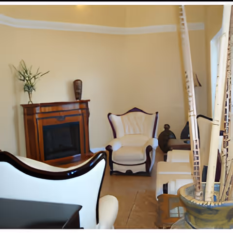A cozy living room with cream-colored walls and beige carpet. The room features a wooden electric fireplace with a decorative vase and plant on top. There are two white upholstered armchairs with dark wood trim, a small side table, and a large decorative vase with tall wooden sticks in the foreground.