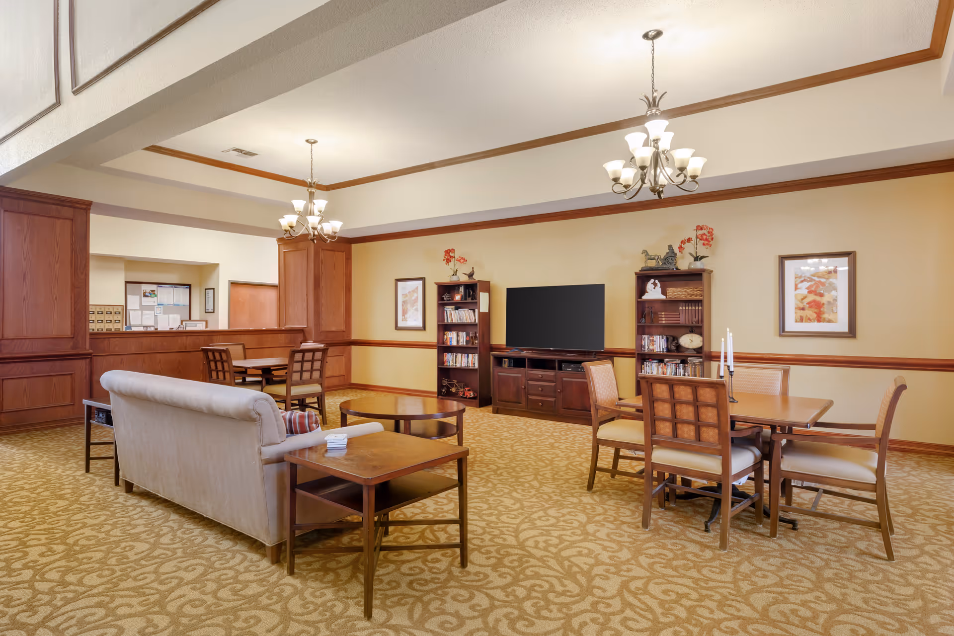 Spacious communal living room with sofas, tables, chairs, bookshelves and a TV under chandeliers.